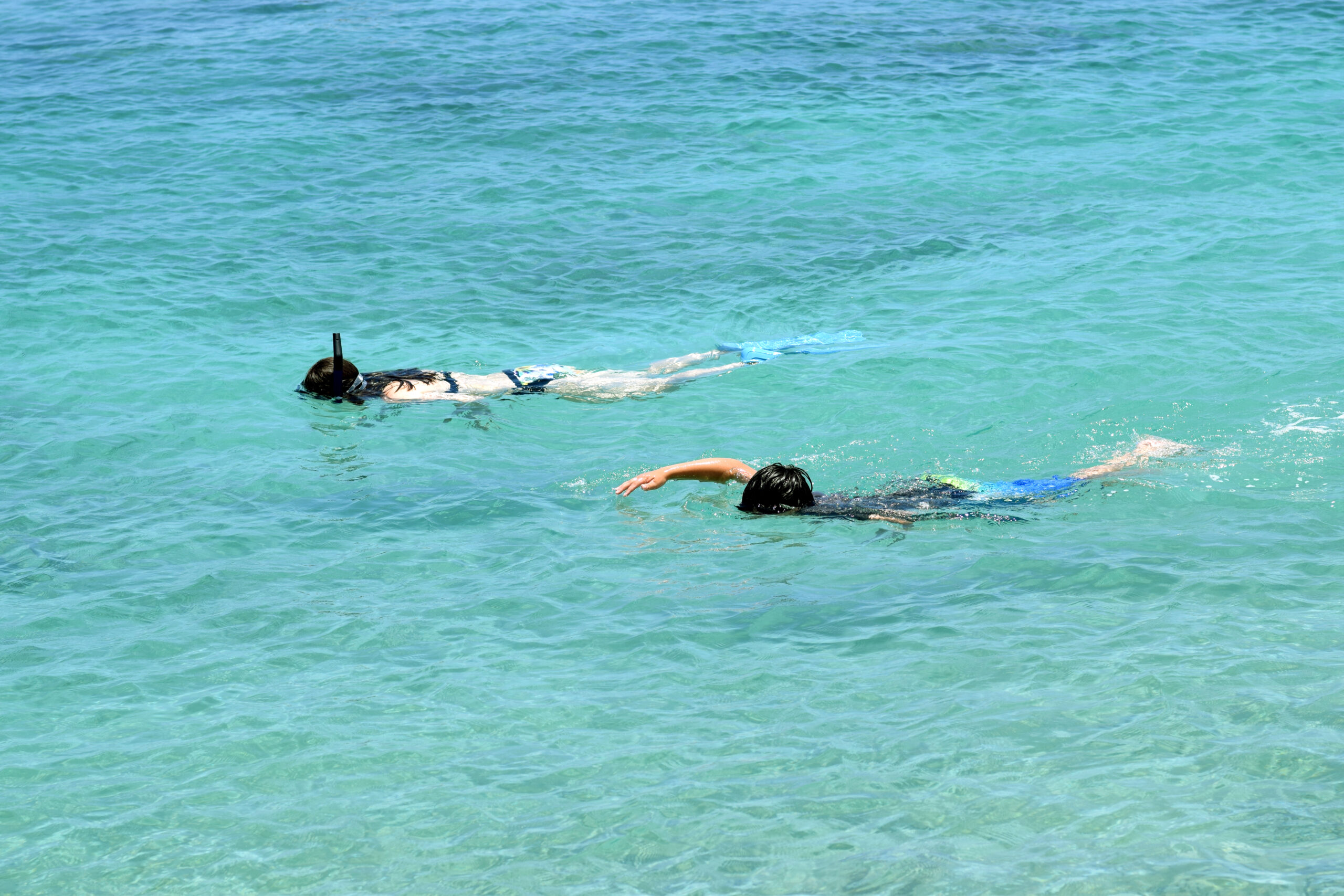 two kids snorkeling in the turquoise water of Makaiwa bay, Big Island, Hawaii